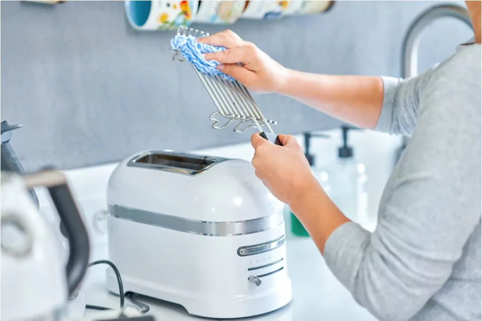 a woman cleaning the tray of a toaster