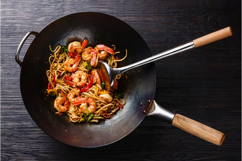 a stir fry pan with noodles and a spatula for stirring