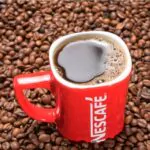 red mug of nescafe on the background of scattered coffee beans