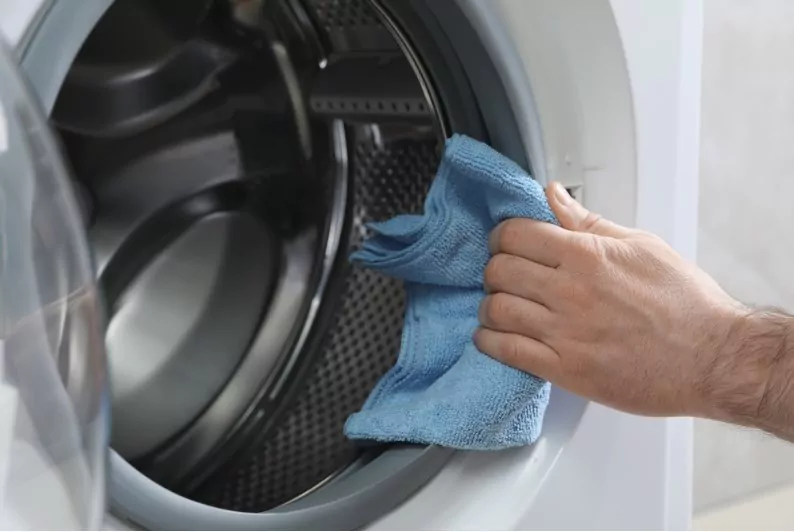 a man wiping and drying washing machine tub with a cloth