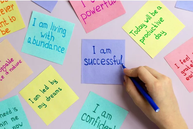 man writing positive affirmations on different coloured papers