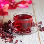 red hot hibiscus tea in a glass mug on a wooden table among rose petals and dry tea custard with metallic heart