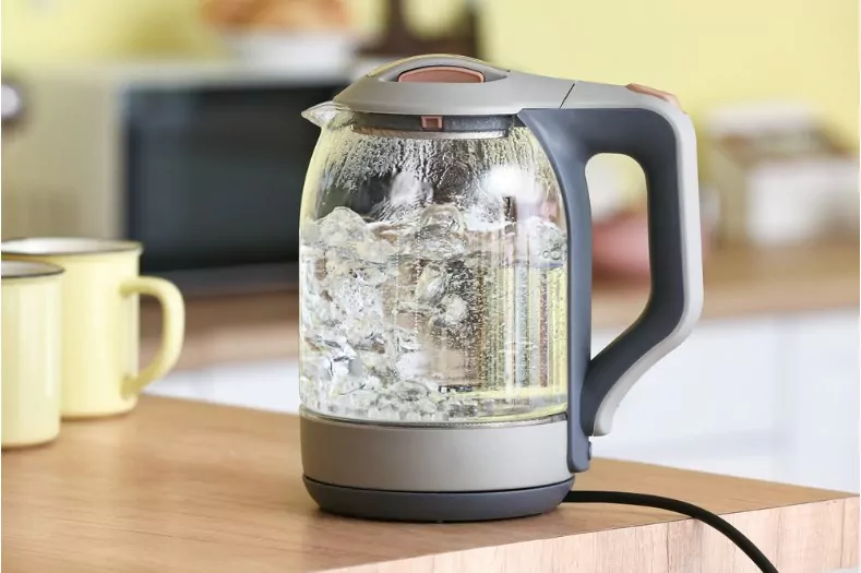 electric kettle with boiling water and cups on kitchen table