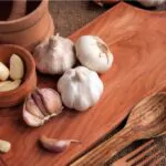 garlic bulb in wooden bowl place on chopping block on vintage wooden background.