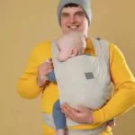 father holding his child in sling on beige background