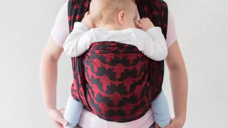 a front view of a babywearing mother carrying her small child in a sling