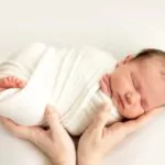 a newborn baby sleeps sweetly in his mother's arms on a white background