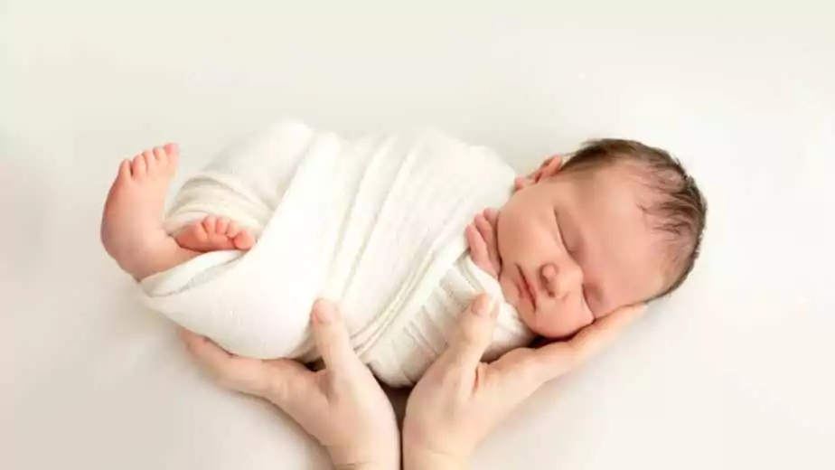 a newborn baby sleeps sweetly in his mother's arms on a white background