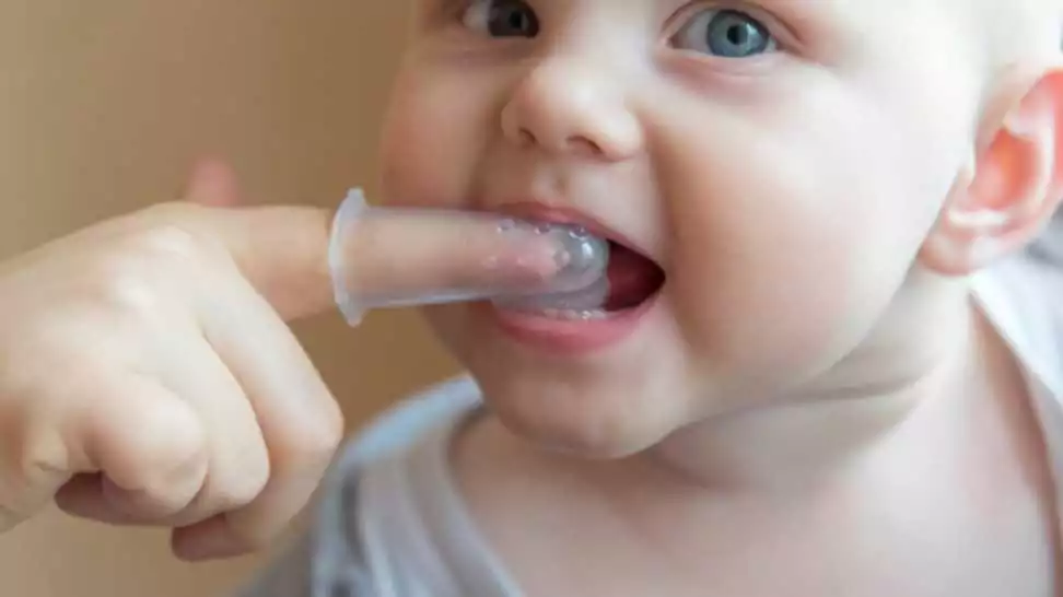 mom brushes baby's teeth with a silicone brush that fits on her finger