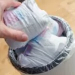 woman hand put used diaper to the trash bin full of used diapers