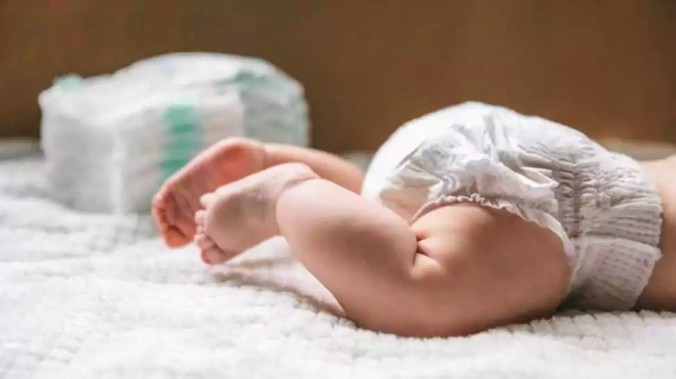 a baby in a diaper at the age of two months and a stack of diapers