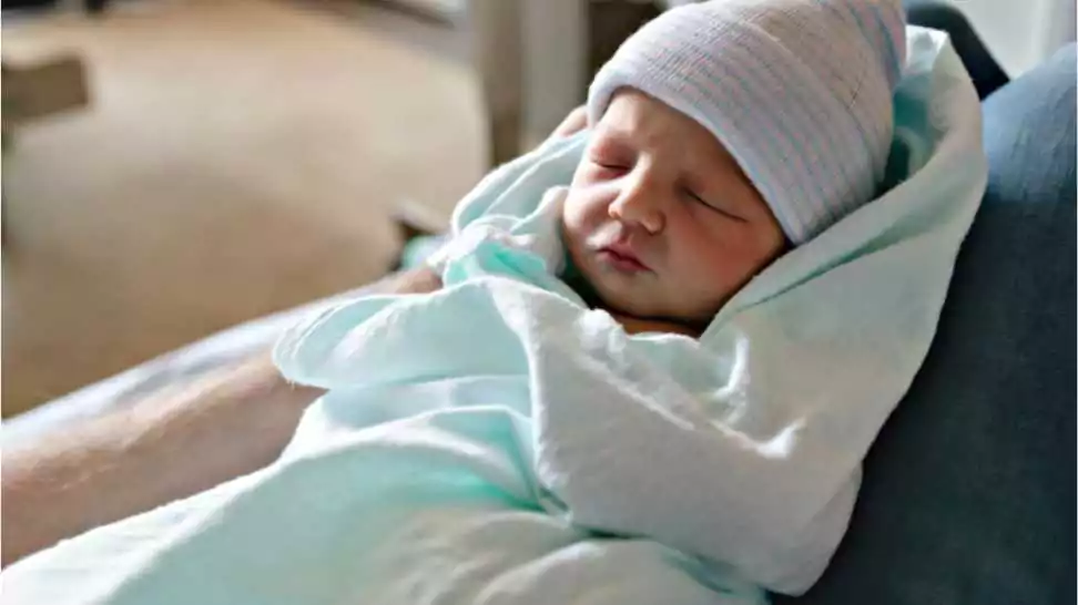 a newborn baby asleep swaddled in hospital blanket and wearing a hat