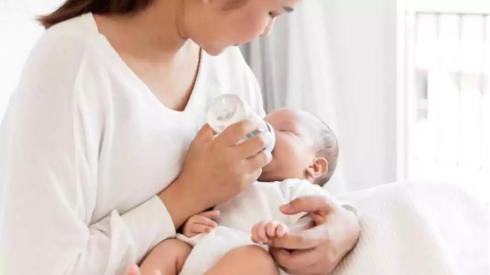 mother breast feeding milk to asian newborn baby on white bed