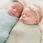 seven week old fraternal twin baby girls swaddled and sleeping on a white flokati rug