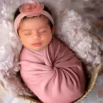 A newborn baby sleeps in a pink cloth wrap blanket on a bed