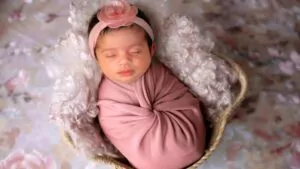 A newborn baby sleeps in a pink cloth wrap blanket on a bed