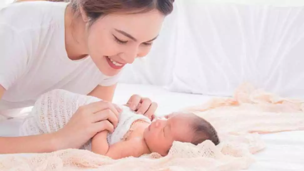 selective focus of asian young mother swaddling baby on bed beautiful woman wrapping adorable infant in thin cloth