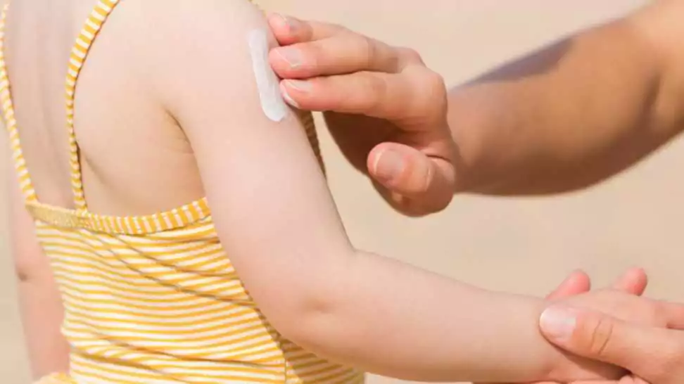 young mother hand applying sunscreen lotion on little girl shoulder