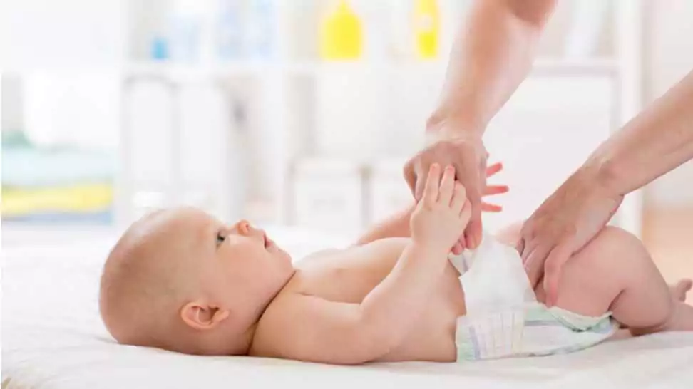 mother putting diaper on her happy baby in nursery
