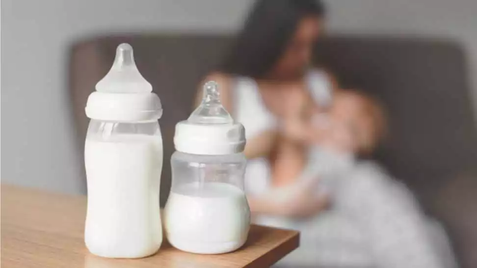 bottles with breast milk on the background of mother holding in her hands and breastfeeding baby