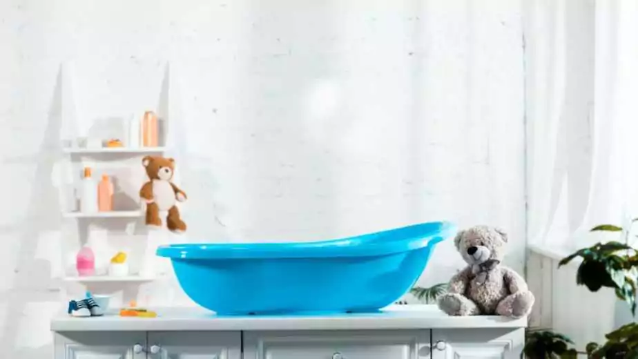 blue baby bathtub near teddy bear and baby sneakers in bathroom