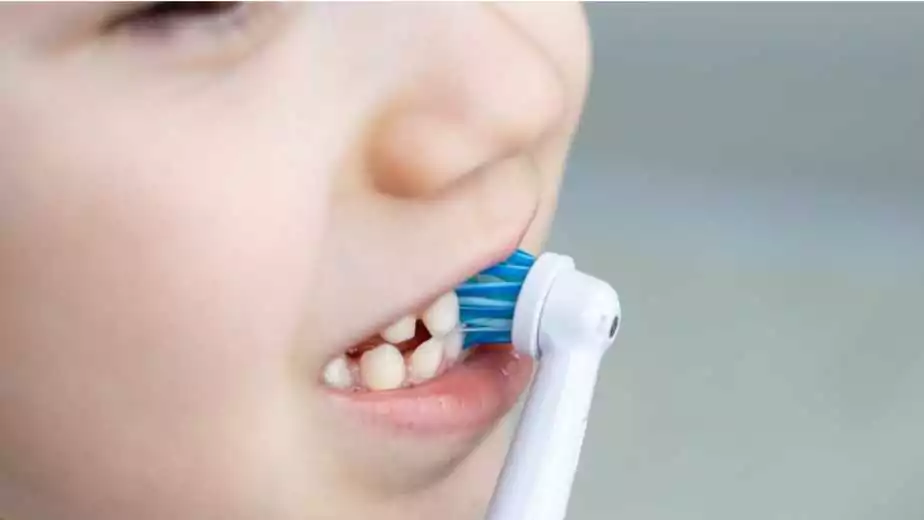 cute kid is brushing his teeth with an electric brush teeth