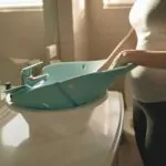 young mom placing baby bath seat into bathroom sink at home