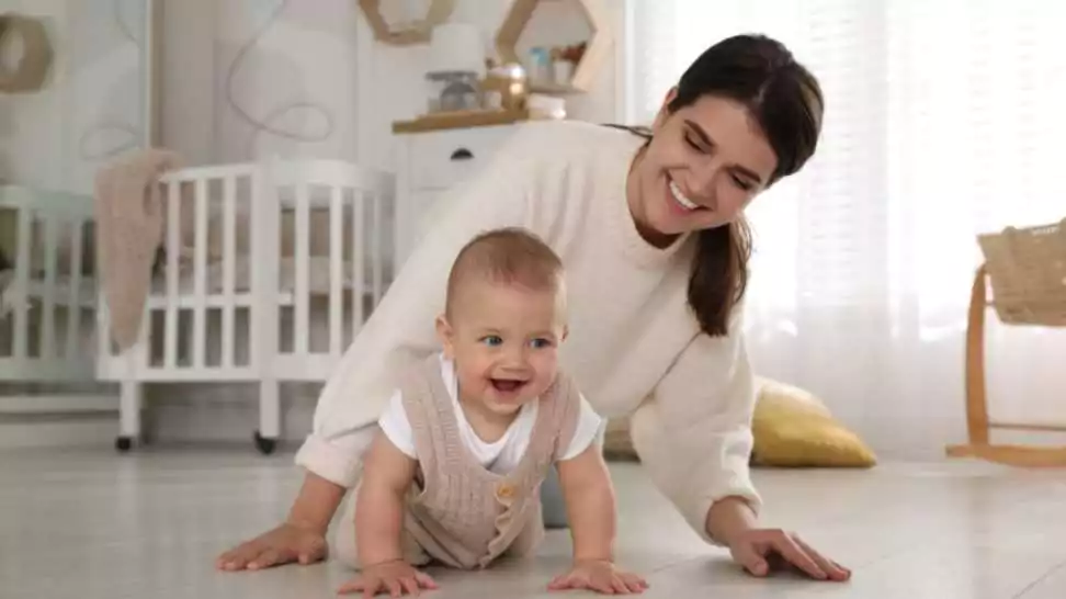 happy young mother watching her cute baby crawl on floor at home