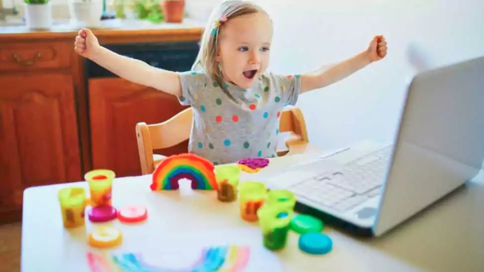 toddler girl playing modelling clay in front of laptop