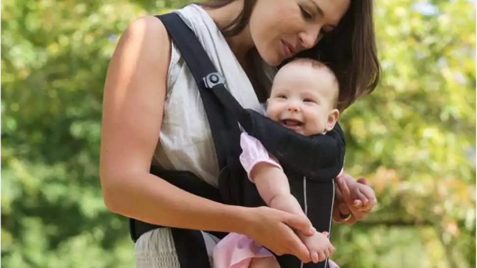 portrait of a happy mother carrying her baby in carrier