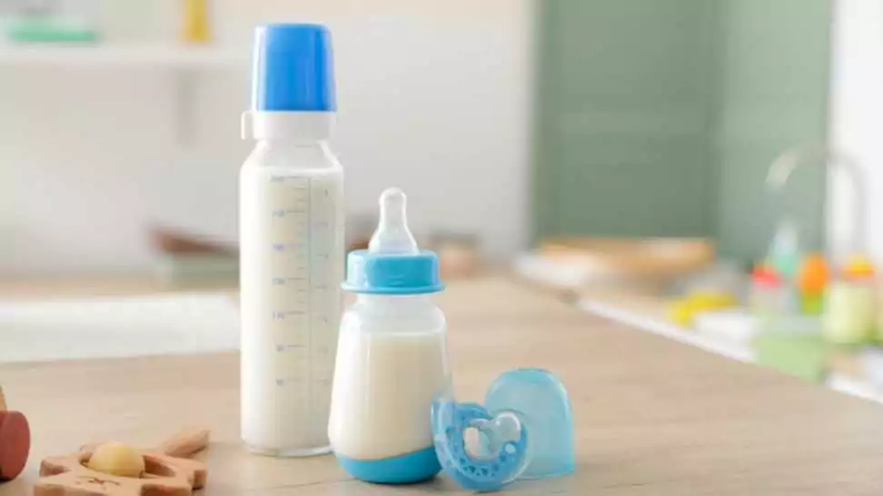 bottles of milk for baby with toys on table in kitchen