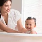 calm asian baby bathing in bathtub enjoys laughing