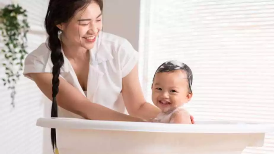 calm asian baby bathing in bathtub enjoys laughing
