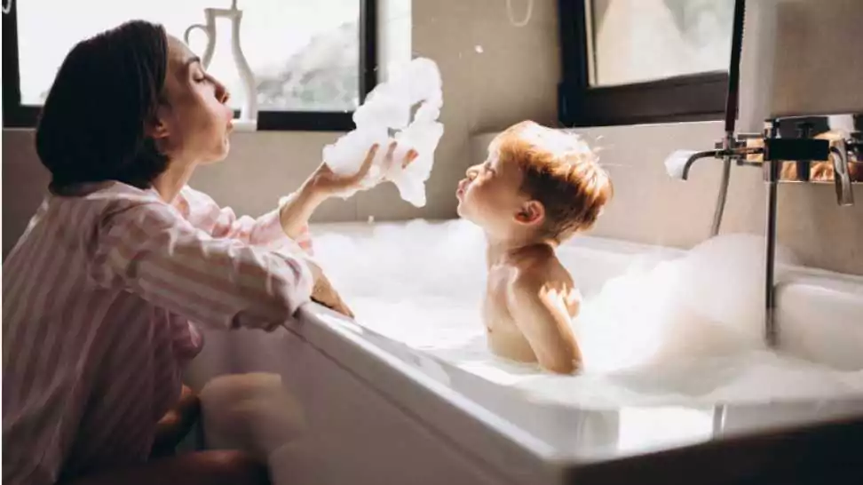 mother playing with her little baby in bathroom while the baby is bathing