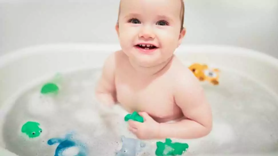 cute little girl playing with rubber toys in small bathtub happy kid having fun while bathing