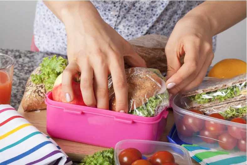 a closeup of hands packing snacks into a pink lunch box