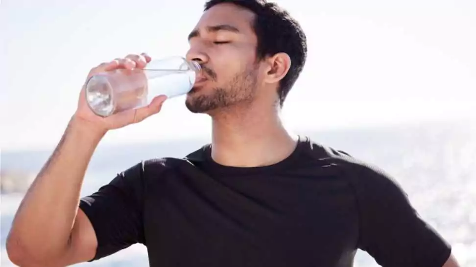 young male athlete hydrating during his workout on the beach