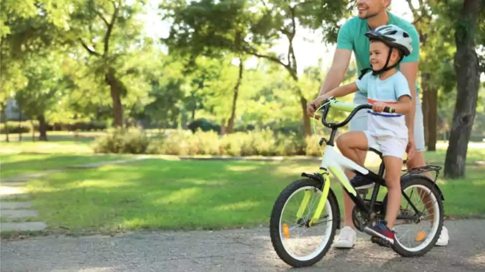 father teaching his son to ride bicycle in park