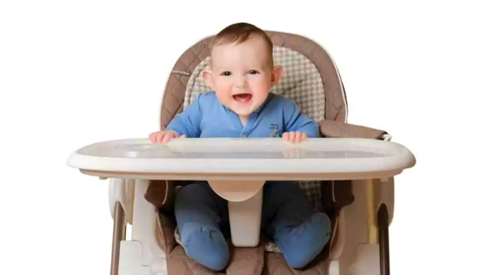 smiling child boy at the age of six months eating while sitting on a high chair