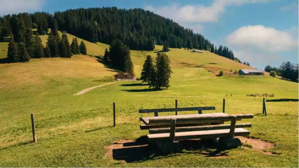 idyllic picnic spot with wooden bench and table with nice view on alpine pastures and hill top in the swiss alps