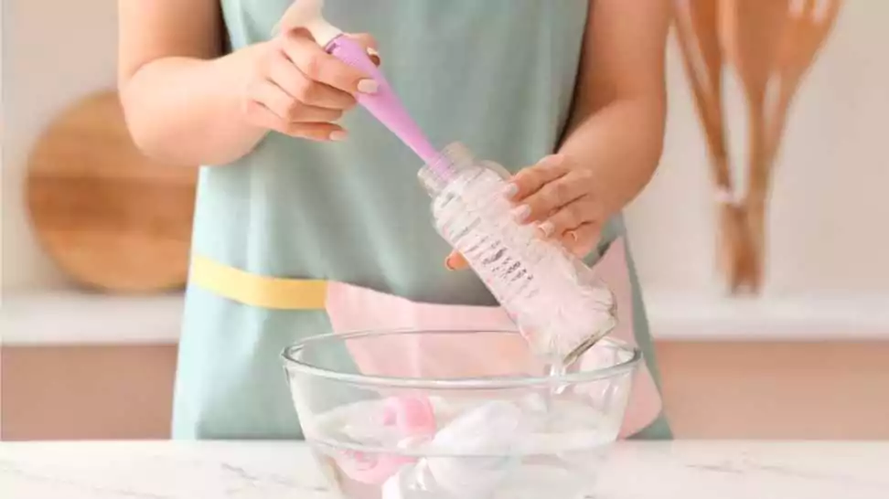 woman cleaning and rinsing a baby bottle at home