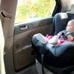 adorable baby girl sitting on an infant car seat and looking outside the window