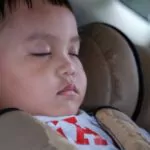 cute little kid sitting and sleeping in a torn infant car chair