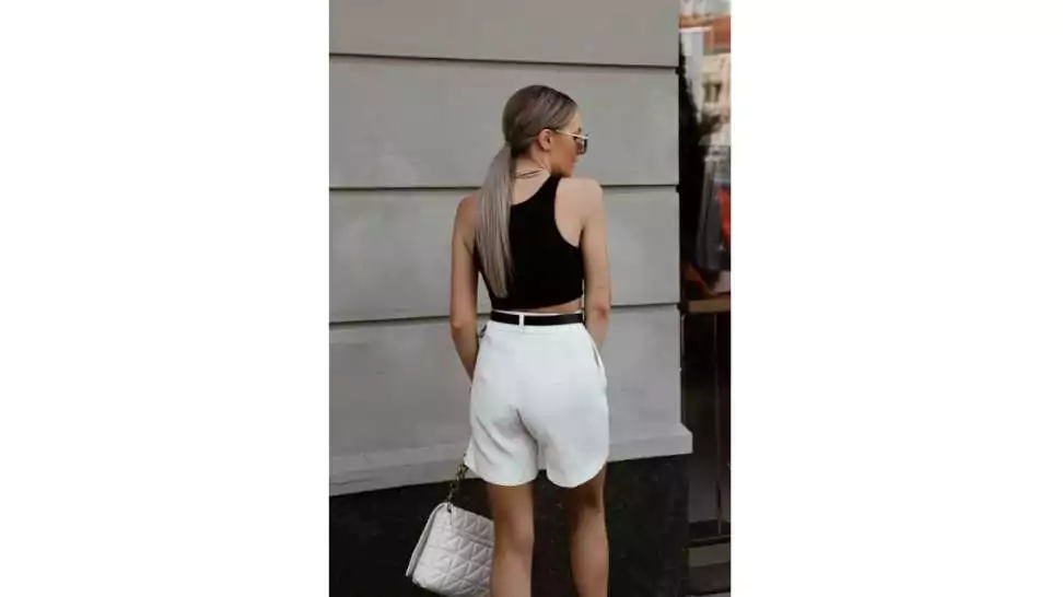 portrait of beautiful young woman dressed in white shorts black tank top mules bag accessories sunglasses belt hair gathered stylish summer fashion outfit lifestyle model