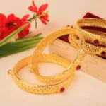 gold indian bangles near a box along with red flowers