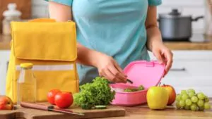 woman packing fresh meal into lunch box in kitchen