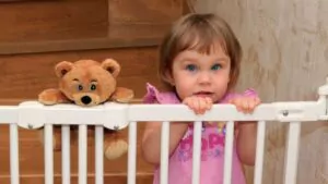 little blonde girl on the stairs with a gate with a teddy bear friend