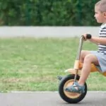 four year old kid playing outdoors on a tricycle