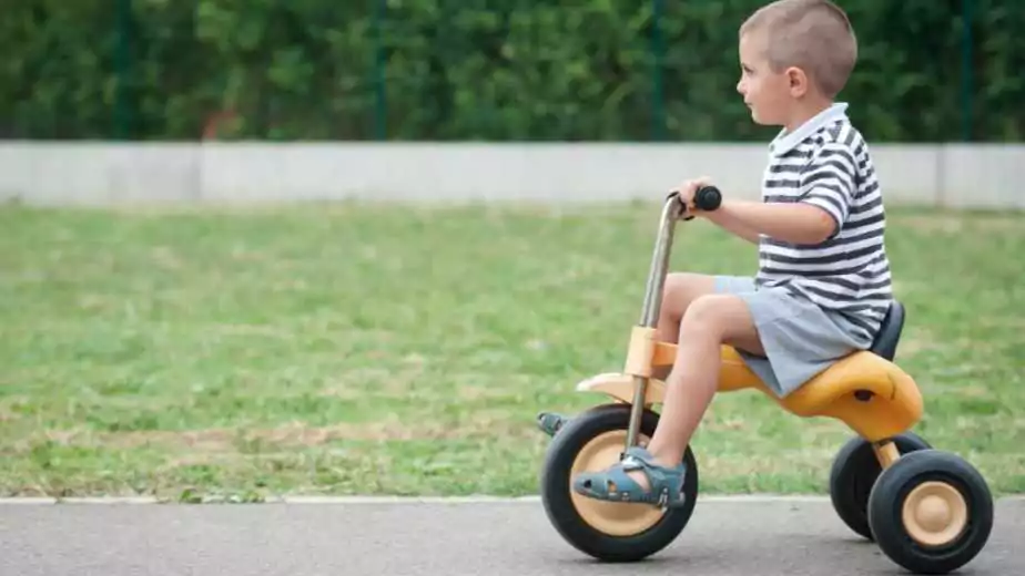 four year old kid playing outdoors on a tricycle