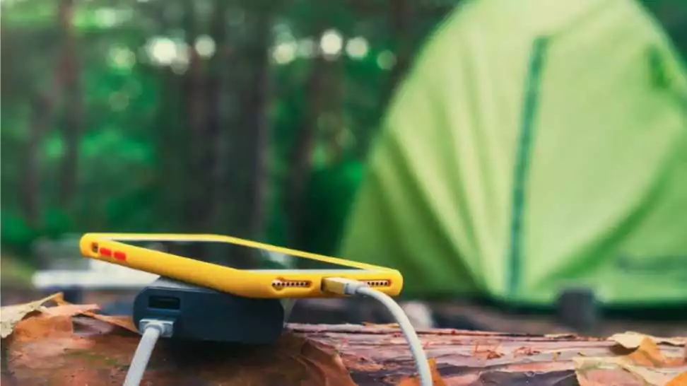 power bank charges the phone outdoors with a backpack against the backdrop of a tent